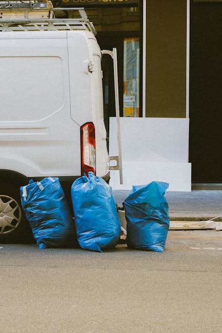 A roadside scene exhibiting a pile of mixed domestic waste, including black plastic trash bags, a yellow plastic container, a worn and discolored car tire, and various small items like paper and packa