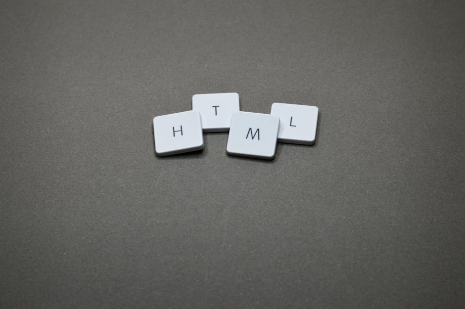 A close-up image features four small, white, square tiles with black letters on each, arranged on a smooth, dark grey surface with a slightly textured finish. The tiles display the letters H, T, M, an
